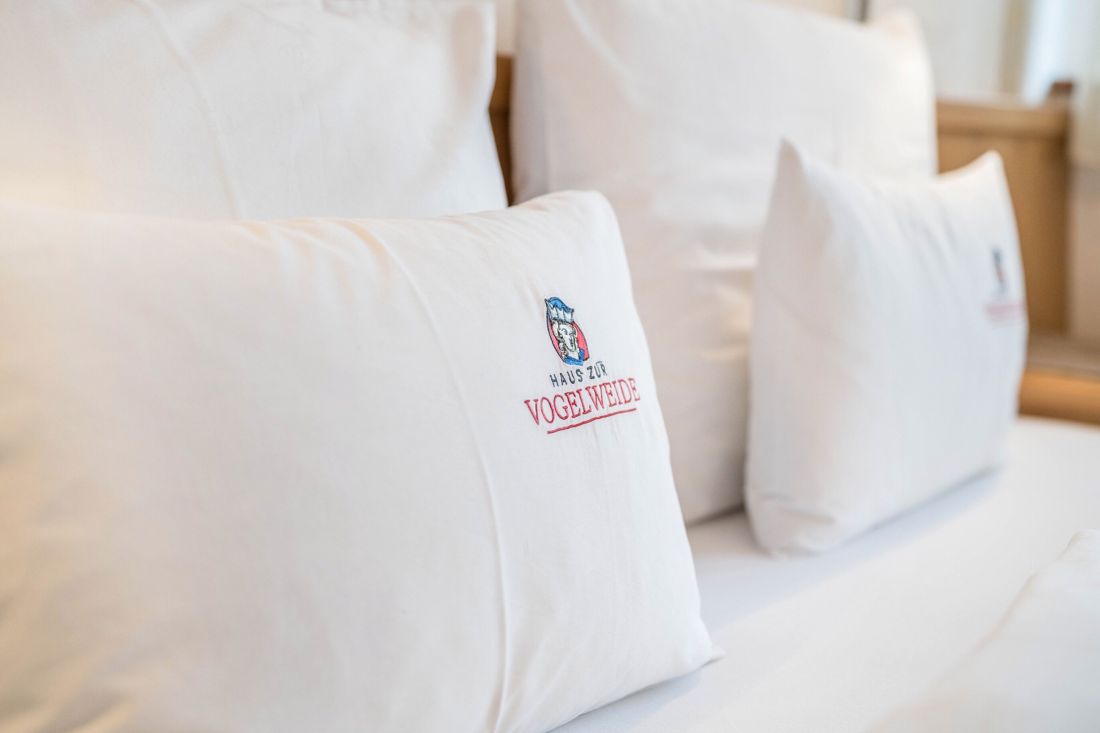 A bed with white pillows, one of which has a logo and text.