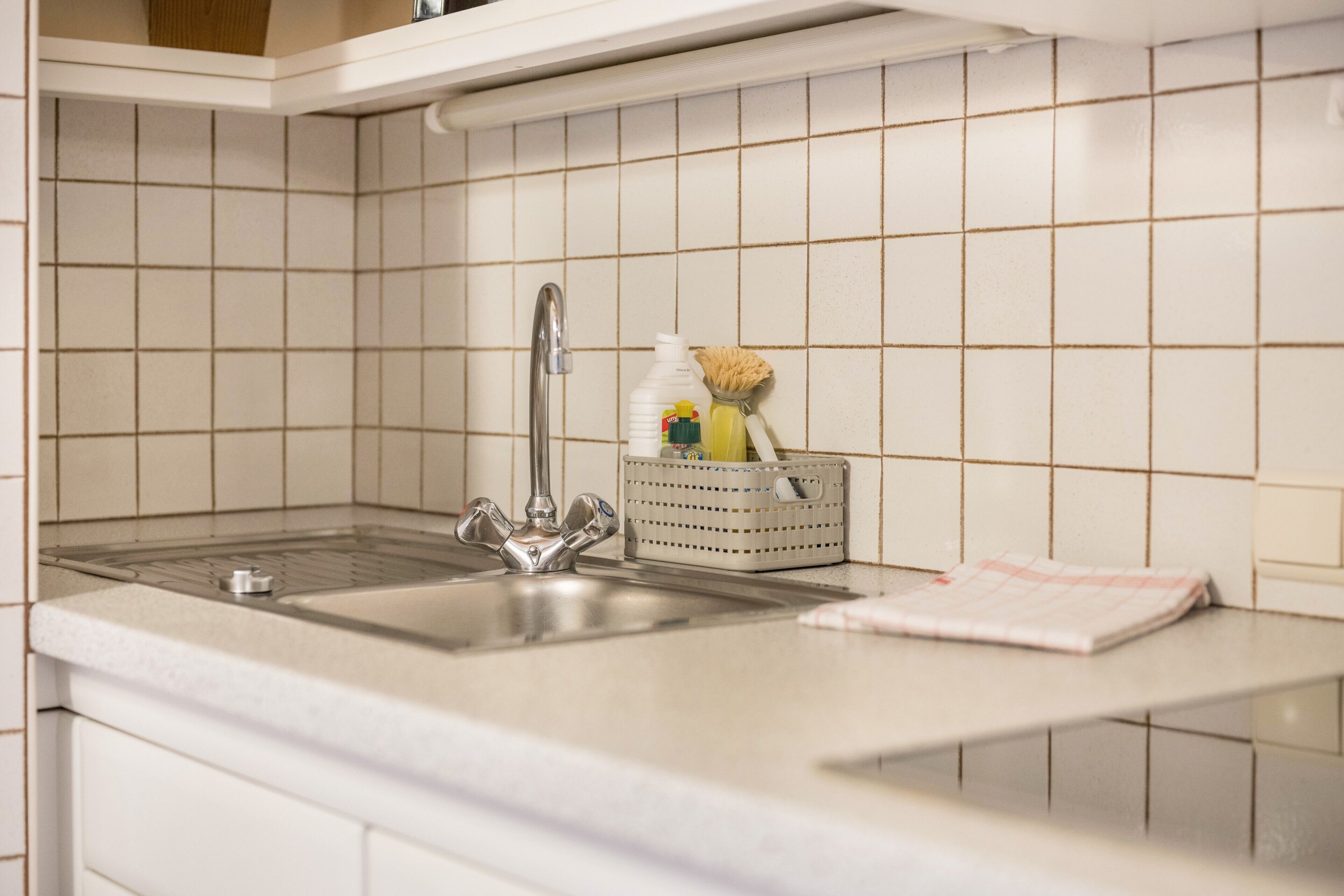 A kitchen with a sink, faucet, and a basket containing cleaning supplies.