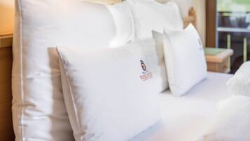 Ett hotellrum med prydligt placerade vita kuddar, en tydlig logotyp på en av kuddarna och ett fönster i bakgrunden.