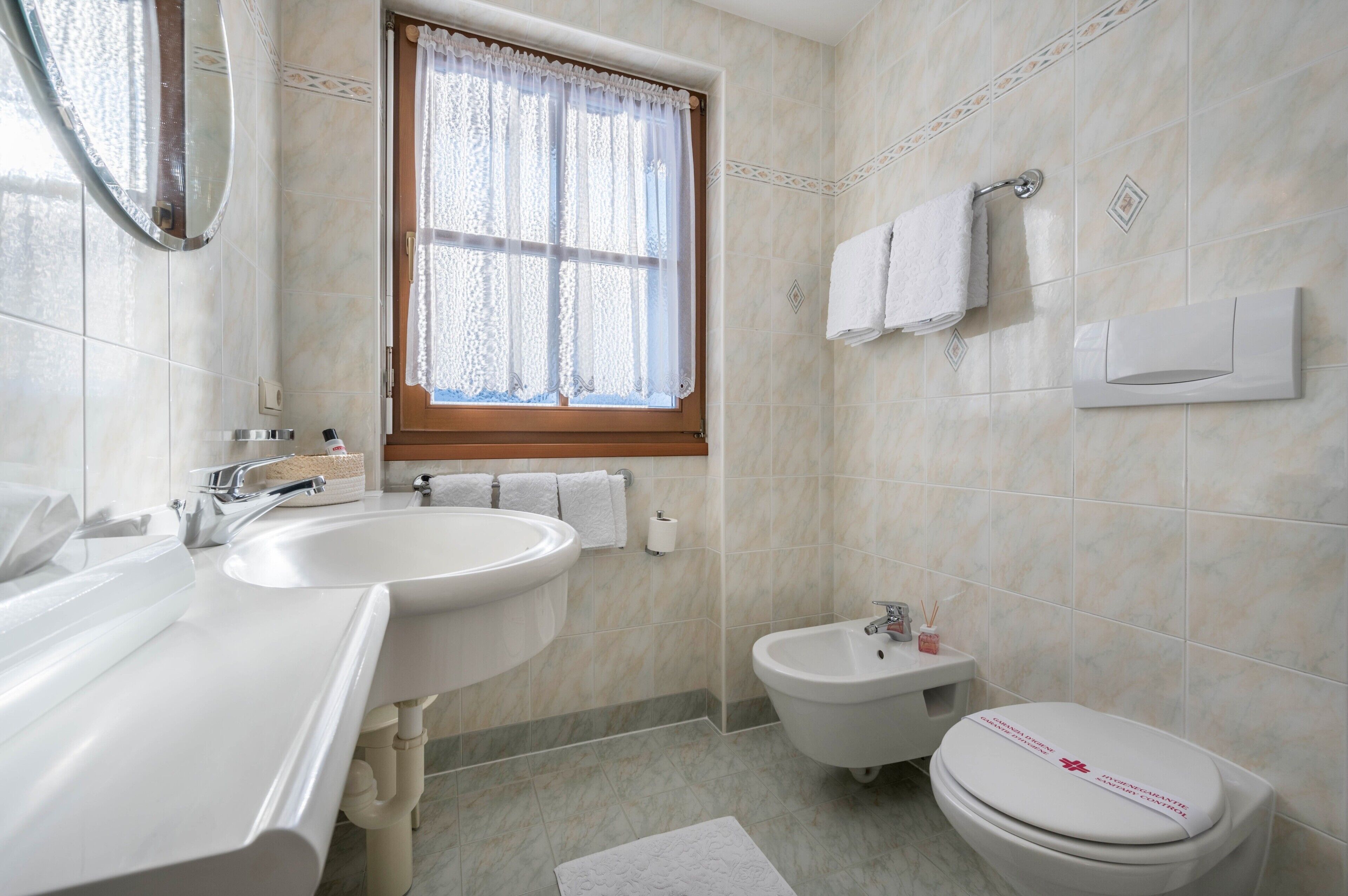 Une salle de bain équipée d’un lavabo, d’un bidet, de toilettes et d’une fenêtre avec des rideaux.