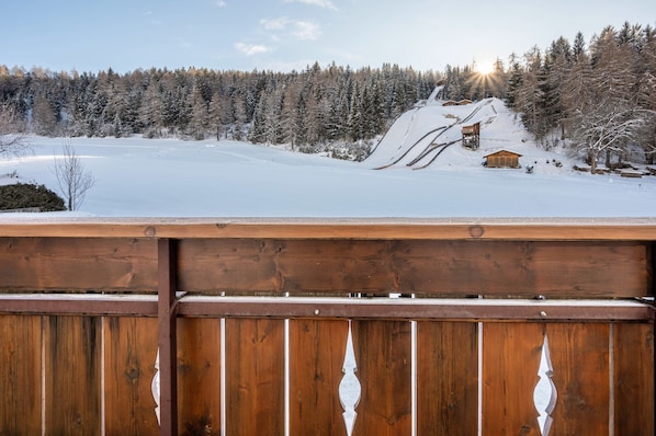 A wooden deck overlooking a snowy landscape with a cabin and a ski lift.