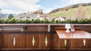 A wooden deck with a table and a lamp, overlooking a residential area with houses and a hilly landscape.