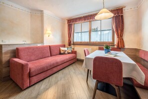Una habitación acogedora con un sofá rojo, una mesa de comedor con sillas, una ventana con cortinas y una lámpara de pared.