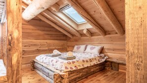 Une chambre dans une cabane en bois, avec un lit en mezzanine, un puits de lumière et un banc en bois rustique.