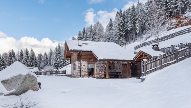 Un chalet en bois avec une façade en pierre, une véranda en bois et un paysage enneigé.