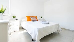 Ein sauberes, weißes Schlafzimmer mit einem Bett, einem Nachttisch, einer Topfpflanze und einem Fenster.