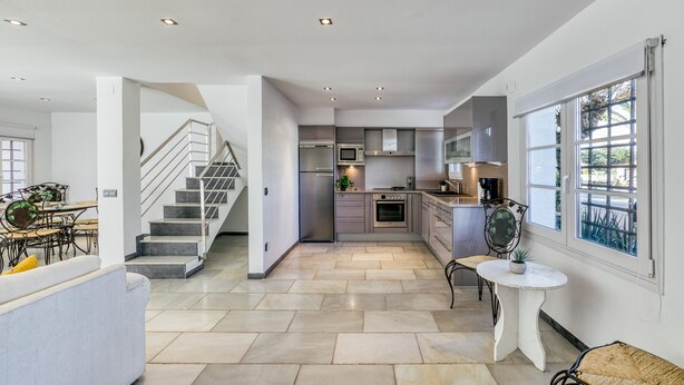A modern kitchen with a central island, built-in appliances, and a dining area with a staircase.