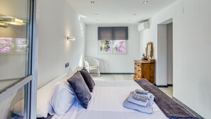 A modern hotel room with a bed, a chair, a dresser, and a window with flowers.