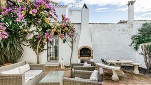 An outdoor patio with wicker furniture, a stone table, and a brick oven.