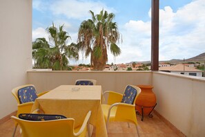 Ein Balkon mit Tisch und Stühlen, einem Blumentopf und Blick auf Palmen und Gebäude.