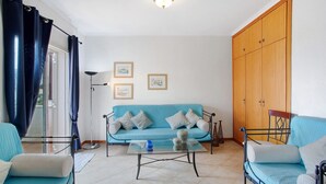 Una sala de estar con sofá, una mesa de centro de vidrio, una cama con estructura metálica y un armario de madera.