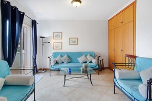 A living room with a sofa, a glass coffee table, a metal-framed bed, and a wooden wardrobe.