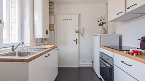 Et kompakt køkken med hvide skabe, en integreret opvaskemaskine, komfur og vask.