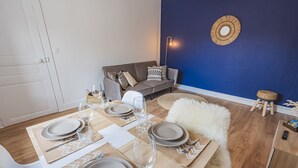 Et spiseområde med et bord dækket til fire personer, en sofa, en blå accentvæg og en lille skammel.