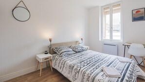 Et soveværelse med seng, sengeborde, en radiator, et vindue og en hængende lampe.