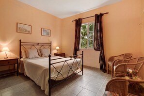 A bedroom with a bed, nightstands, a window with curtains, and wicker chairs.