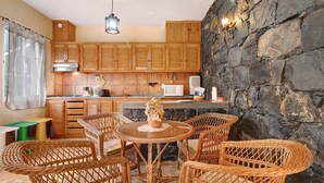 Une cuisine avec des meubles de rangement en bois, un mur en pierre, des meubles en osier et un luminaire suspendu.
