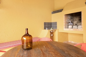 Una mesa redonda de madera con una botella, una silla rosa, un revoque de azulejos y un horno de ladrillo.