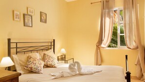 Ein ordentlich bezogenes Bett mit einer herzförmigen Handtuch-Anordnung, einer Nachttischlampe und einem Fenster mit Vorhängen.