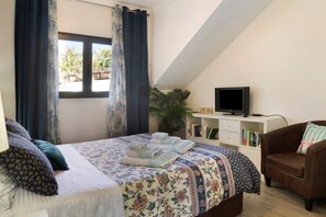 Een slaapkamer met een bed, een televisie, een boekenkast, een stoel en een raam met gordijnen.