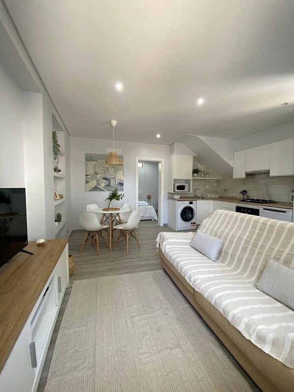 Un salon moderne comprenant un canapé, une table à manger avec des chaises, un téléviseur et un coin cuisine équipé d’appareils électroménagers.