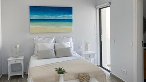 Een slaapkamer met een bed, nachtkastjes, een bankje, een schilderij en uitzicht door een raam.