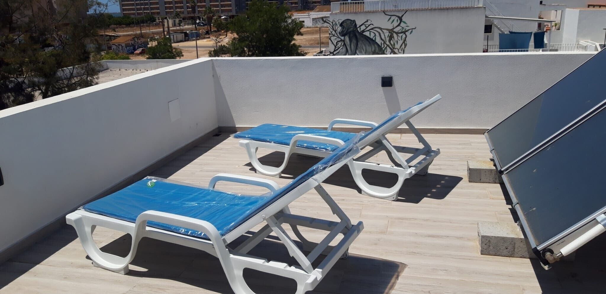 Une terrasse sur le toit avec trois chaises longues, un chauffe-eau et une vue sur les bâtiments environnants.