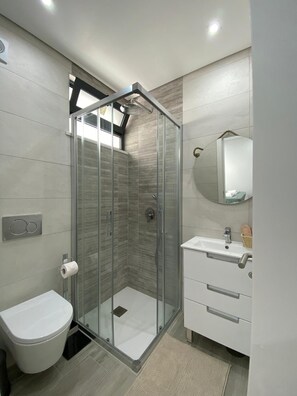 Une salle de bain moderne avec une douche à parois de verre, des toilettes, un lavabo avec un miroir et un petit meuble de rangement.