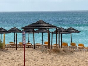 A beach with umbrellas and chairs, a no swimming sign, and the ocean in the background.