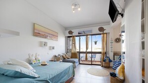 Une chambre avec un lit, une télévision, une fenêtre avec des rideaux et un balcon avec des chaises.