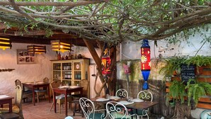 Un café en plein air avec des tables et des chaises, un buffet en bois contenant des bouteilles et un panneau indiquant la présence d’un distributeur automatique sans système de dépôt de bouteilles.