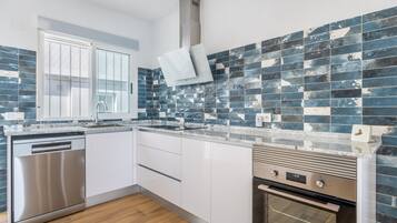 Una cocina moderna con armarios blancos, lavavajillas de acero inoxidable, horno empotrado y salpicadero con azulejos azules.