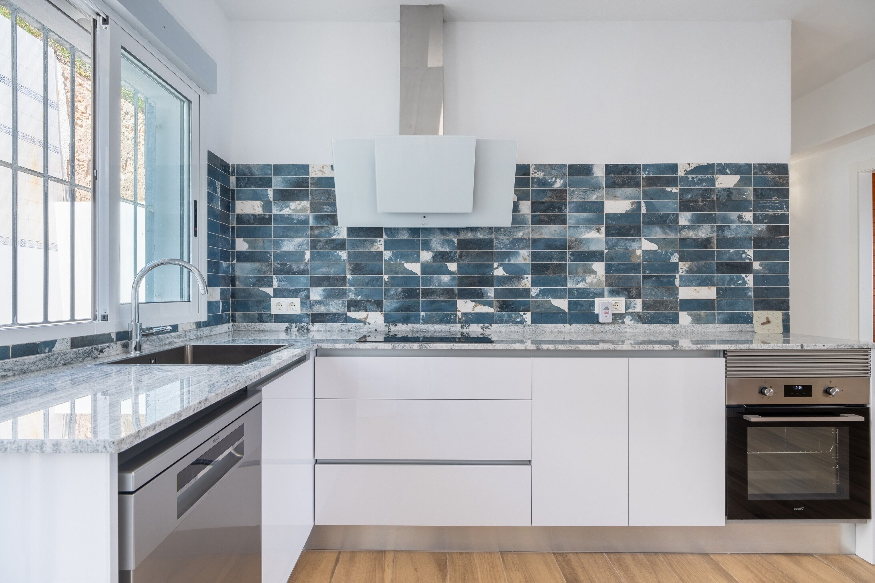 Een moderne keuken met een groot eiland, roestvrijstalen apparatuur en een spatwand met blauwe en witte tegels.