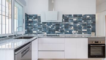 Een moderne keuken met een groot eiland, roestvrijstalen apparatuur en een spatwand met blauwe en witte tegels.
