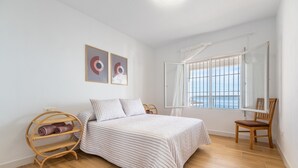 A bedroom with a bed, a wooden chair, a shelf with towels, and a window with a view. - Holiday Home 'Posidonia' with Sea View, Private Terrace and Wi-Fi (Torrevieja)