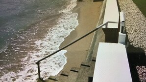 Una escalera que baja a una playa de piedras y olas.