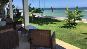Un espacio al aire libre techado con mobiliario de mimbre, un césped y vistas a la playa y al océano.