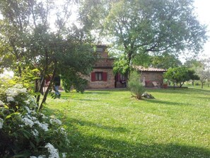 Un edificio in pietra con tetto rosso, immerso in un'area verde con alberi e fiori.