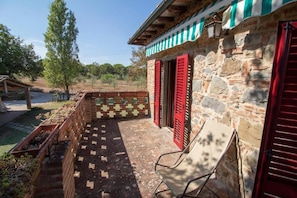 Un bâtiment en pierre avec des volets rouges, une terrasse carrelée et un banc en bois.