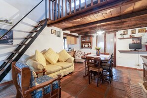 Un escalier en bois, un canapé, une table à manger avec des chaises et un téléviseur, le tout dans un décor rustique.