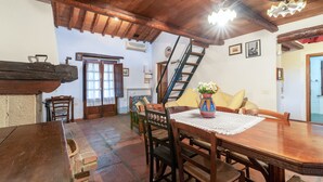 Un comedor con una mesa de madera, sillas, un florero con flores, una escalera y una puerta.