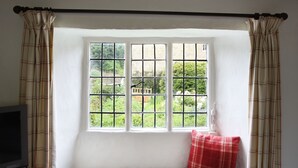 Ein Fensterplatz mit kariertem Vorhang, einem Fernseher auf einem Schrank und einem roten Kissen.