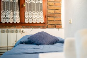 Un lit avec un matelas bleu et un oreiller bleu foncé, une porte en bois avec un rideau en dentelle et un mur de briques.
