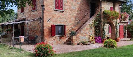 A stone building with red shutters, a covered patio, and a grassy yard.