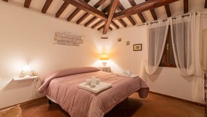 Une chambre avec un plafond en bois, un lit avec une literie rose, une table de chevet avec une lampe et une fenêtre avec des rideaux légers.