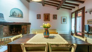 Un coin repas avec une table en bois, des chaises, un vase de fleurs, une cheminée et des tableaux encadrés au mur.