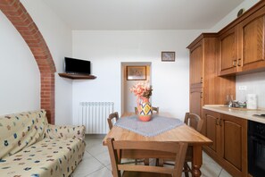 A dining area with a wooden table, chairs, a TV mounted on a brick wall, a radiator, and wooden cabinets.
