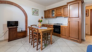 A kitchen with wooden cabinets, a dining table with chairs, a TV, and a brick fireplace. - Apartment “Papà Giuseppe La Stalla” with Shared Pool and Wi-Fi (Cortona)