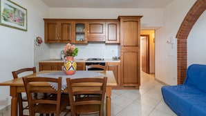 A kitchen with wooden cabinets, a dining table with chairs, a blue sofa, and a tiled floor. - Apartment “Papà Giuseppe La Stalla” with Shared Pool and Wi-Fi (Cortona)