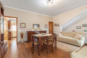 A dining area with a wooden table and chairs, a sofa, and a patterned rug.